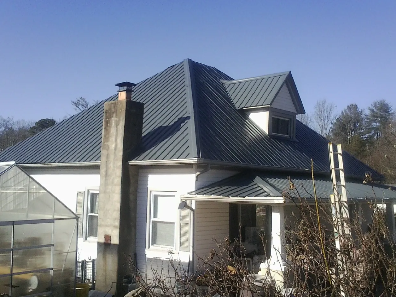 Dark blue standing seam metal roof on a white farmhouse with dormer — Slate & Tile Roof Repair by Roofing Brothers in Downey