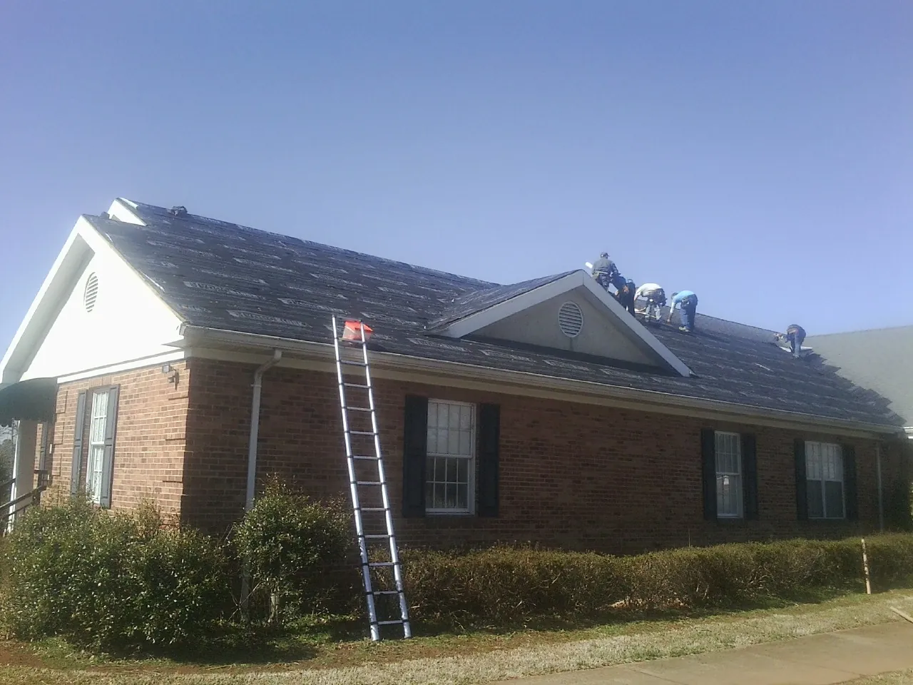 Crew tearing shingles off a brick ranch roof with a ladder set — Emergency Roof Repair work by our crew in Downey