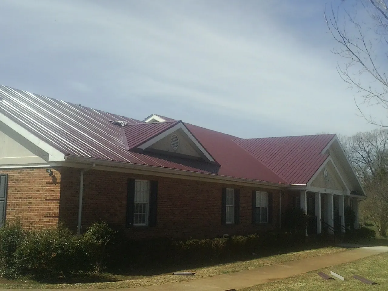 Red metal roof with gabled entries on a long brick building, from a Hail Damage Roof Repair job in Downey