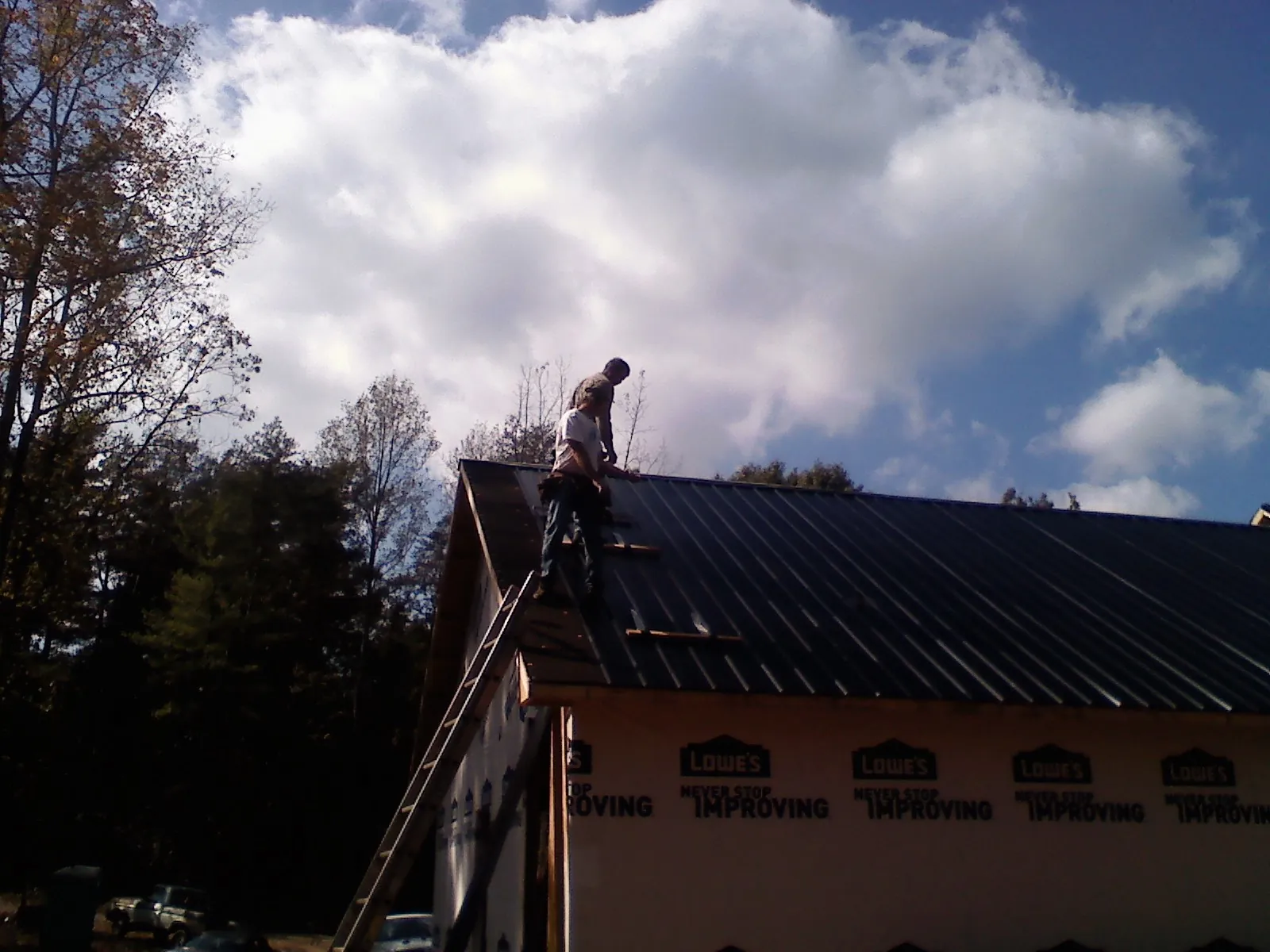 Roofer fastening dark metal panels high against a cloudy sky, from a Roof Inspection job in Downey