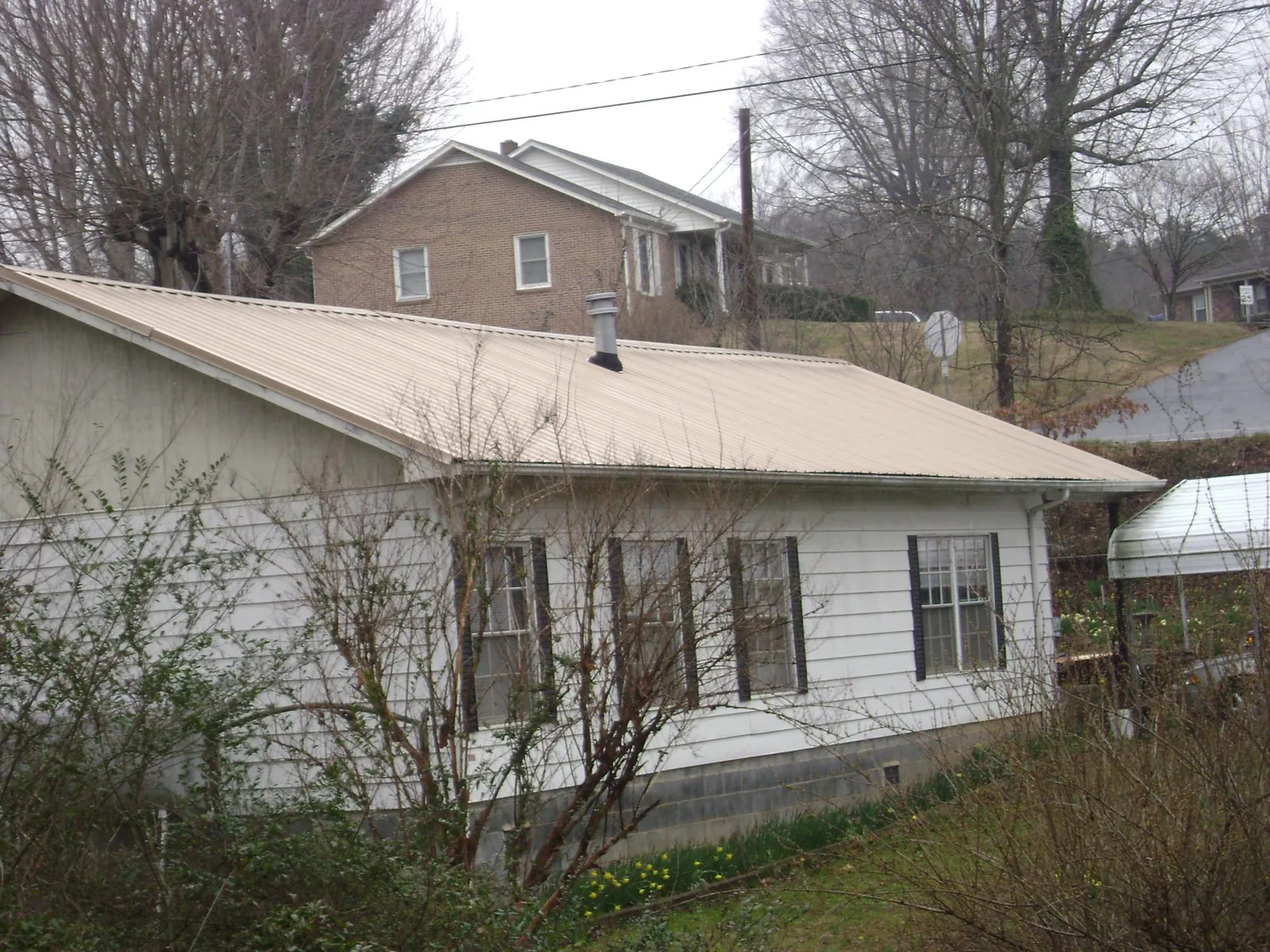 Tan metal roof on a white sided house set into a hillside — Commercial Roofing by Roofing Brothers in Downey